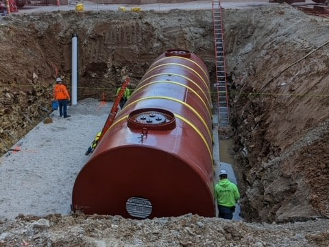 Underground steel storage tank being installed in a large excavation with workers onsite.